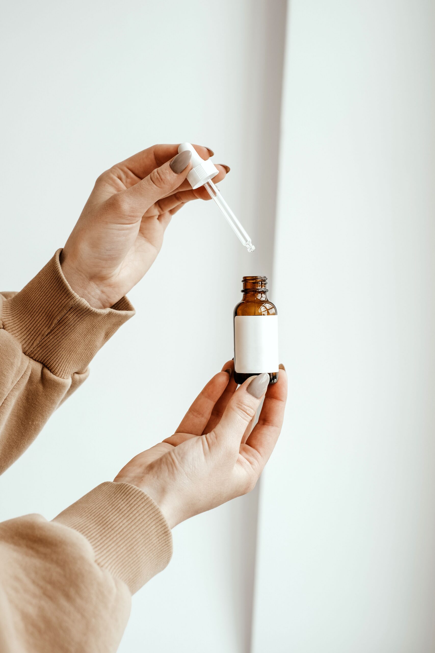 Hands checking a blank-label amber dropper bottle for a private label morning facial oil sample