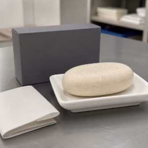 Pale oval body cleansing bar sample beside a blank carton on an illustrative OEM review table