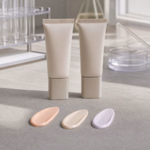 Unbranded sheer tone-adjusting skin-prep cream samples and three undertone swatches on a cosmetic factory sample table